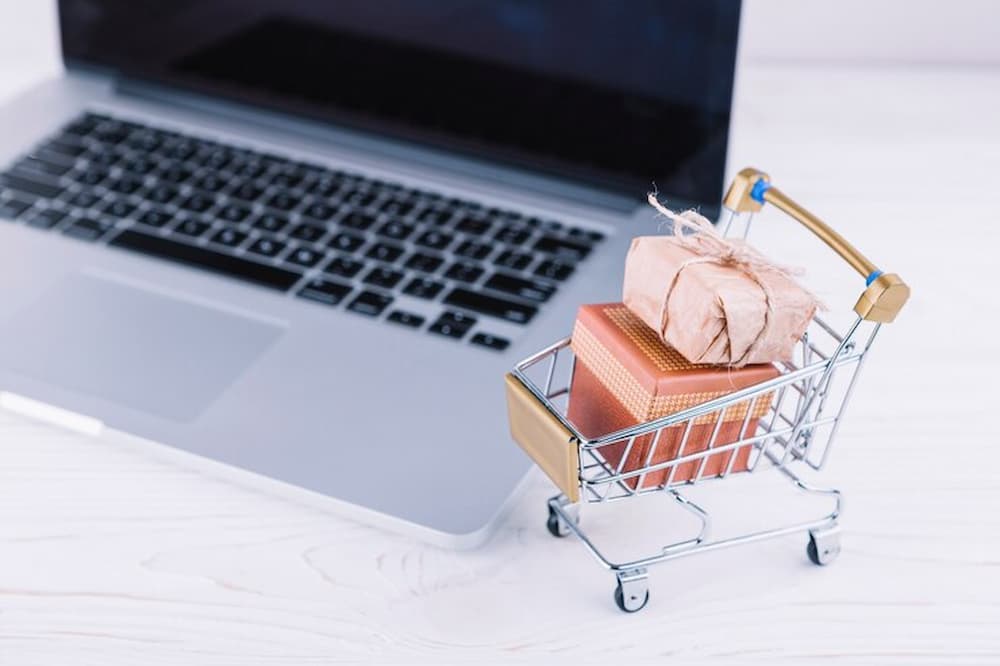 pequeño carrito de supermercado con regalos junto a laptop